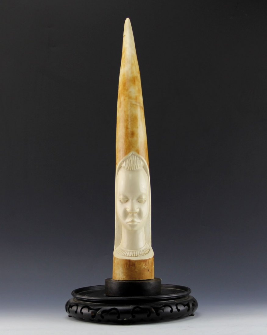 AFRICAN IVORY TRIBAL CARVING ELEPHANT TUSK: AFRICAN IVORY TRIBAL CARVING ELEPHANT TUSK Antique African carved ivory tusk; two toned with highly polished sunk relief of female face. Attached to open work wood base. Weight: 5.6 lbs with base Size