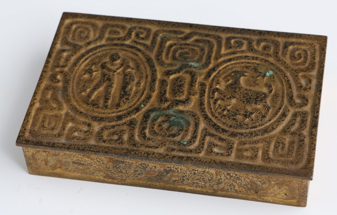 TIFFANY STUDIOS DRESSER TRINKET BOX: TIFFANY STUDIOS DRESSER TRINKET BOX Tiffany Studios dresser trinket box. Made of gilt iron. Design consists of stylized imagery. Stamp on the bottom reads "Tiffany Studios / New York / 810". Size: 5.2