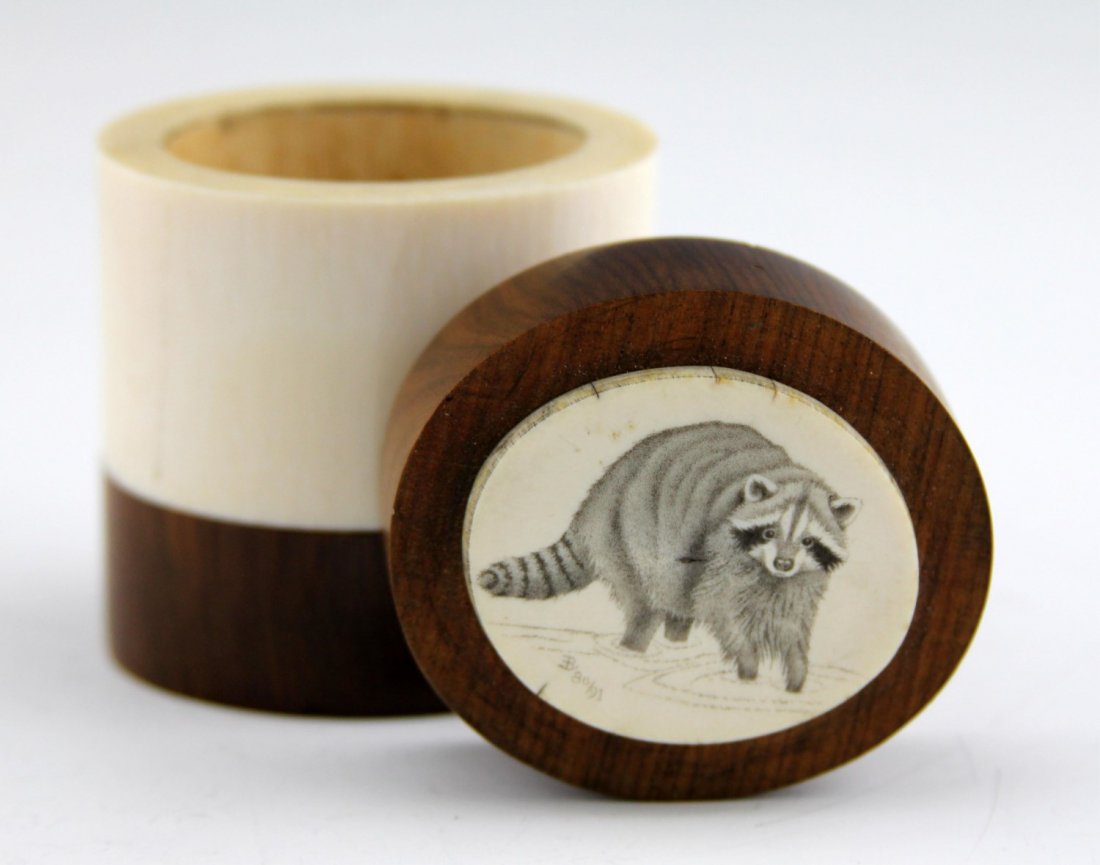 IVORY & WOOD SCRIMSHAW TRINKET DRESSER BOX: IVORY & WOOD SCRIMSHAW TRINKET DRESSER BOX African ivory and wood dresser trinket box with monochrome scrimshaw of raccoon on underside of lid. Signed "B 80/91." Weight: 170.3g Size: 2.25 x 3"