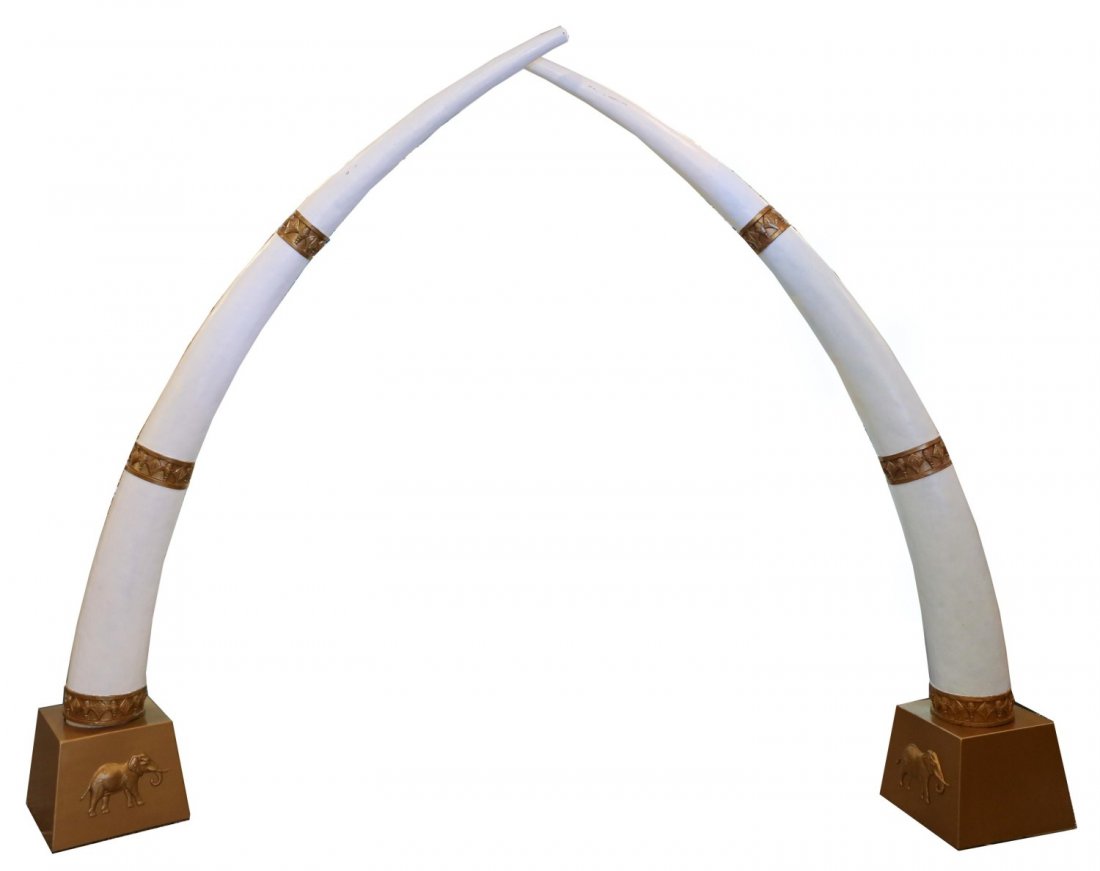PAIR OF GIANT FAUX TUSKS WITH GILT ACCENTS 9': PAIR OF GIANT FAUX TUSKS WITH GILT ACCENTS 9' Giant fair of faux tusks, accented with gilt bars and set onto gilt stands with elephant accents. Stand measures 15" square, tusks are approximately 9' ta