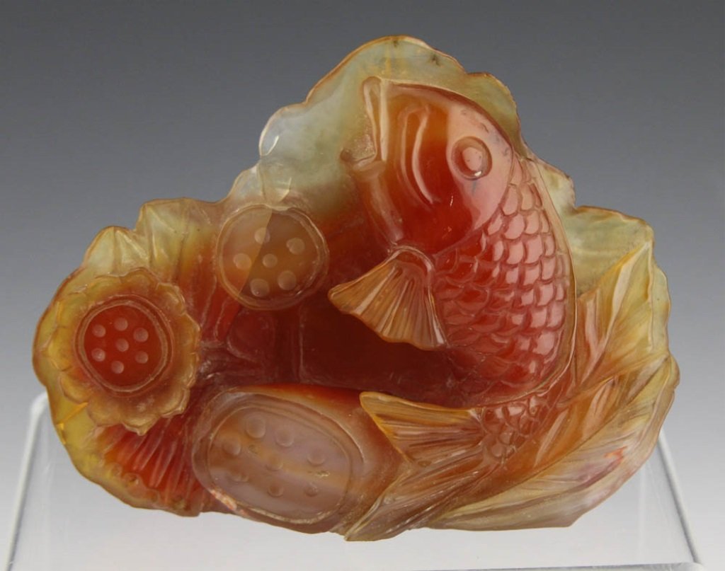 CHINESE CARVED CARNELIAN AGATE CARP W LOTUS PODS: CHINESE CARVED CARNELIAN AGATE CARP W LOTUS PODS Chinese carved carnelian agate depicting a leaping carp against lotus pods. Unmarked. Weight: 583.1g Size: 5.5 x 4.5"