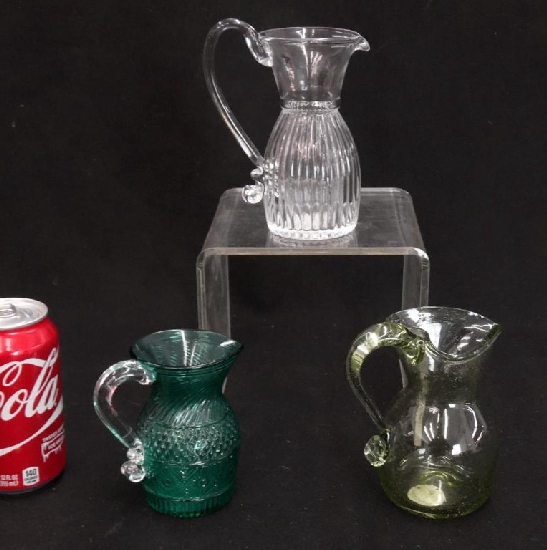 Glassware Lot: Lot (3) pieces including (2) Pairpoint blown glass creamers and light green Historic Jamestown blown glass Colonial style creamer with original tag and receipt. 4 1/4" to 6" Ht..