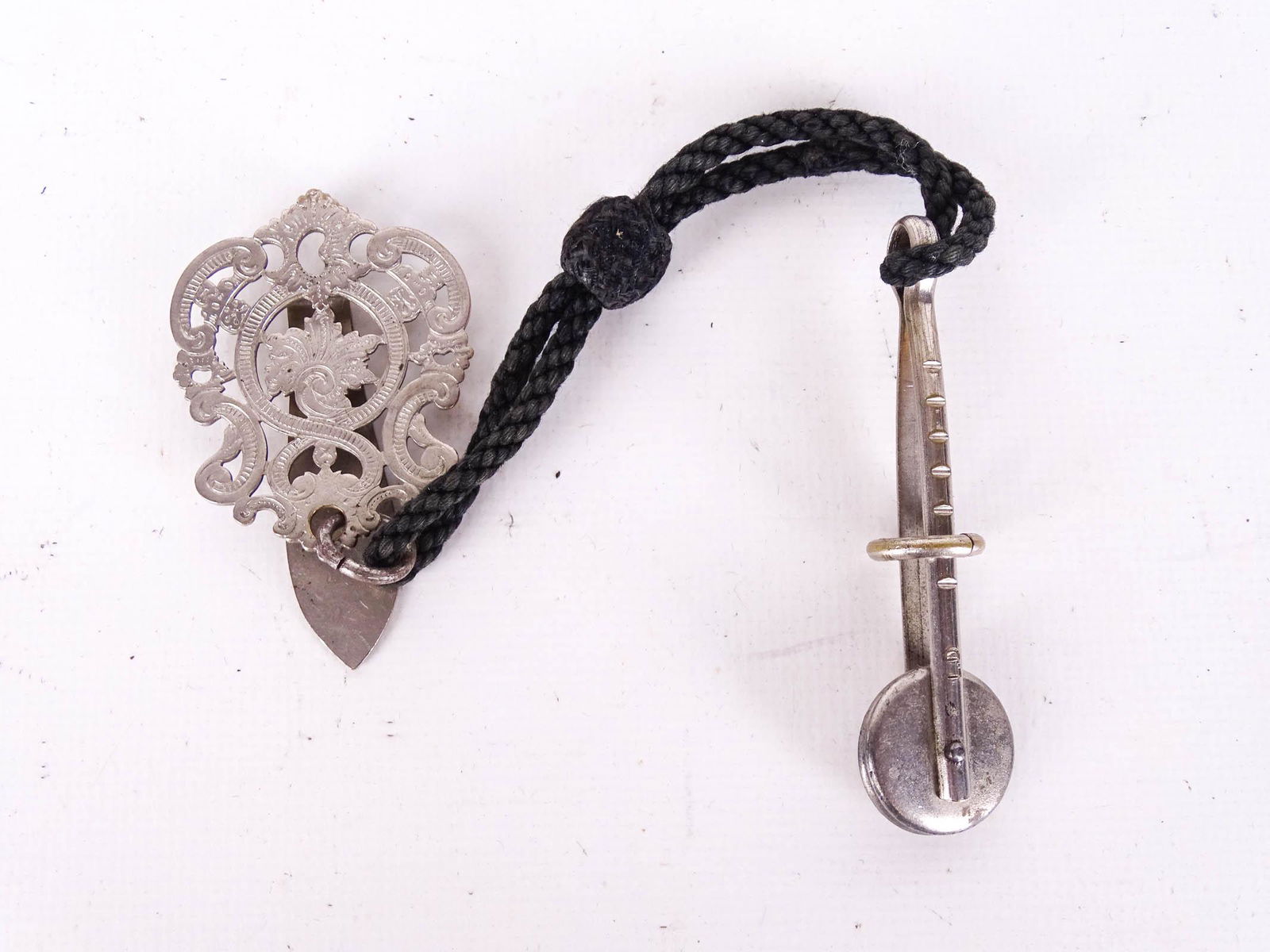 C. 1890 Skirt Clip: Skirt Clip. Ladies Victorian antique vanity object. Nickle plated foliate pierced clip to fit on belt. Original cord. Clip marked “L.D”. 9-1/4” long. Very good overall.