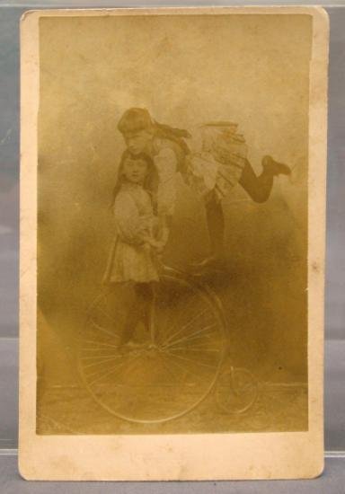 Photograph, Cabinet Card: Photograph, Cabinet Card of a young Lady doing a single leg seat stand on a High Wheel bike while another young lady is standing on the pedals. Circa 1886. Size is 4-1/4" x 6-1/2". Unusual lady trick 