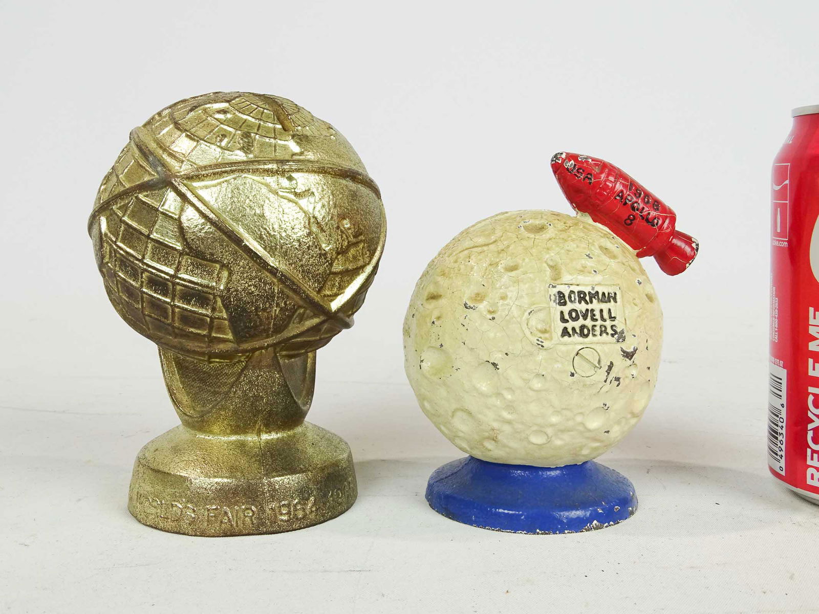 Bank Lot: Lot (2) banks including white metal Unisphere (5" Ht., 1964, #802 Penny Bank Book, missing trap), and cast iron Apollo-8 (4 1/4" Ht., 1968, #800 Penny Bank Book, Mfg. John Wright).