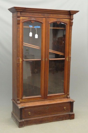Victorian Bookcase: Victorian walnut two door single drawer Eastlake bookcase on stand with carved elements above doors. 48" W 16" D 65" Ht. some damage lower left side of case.