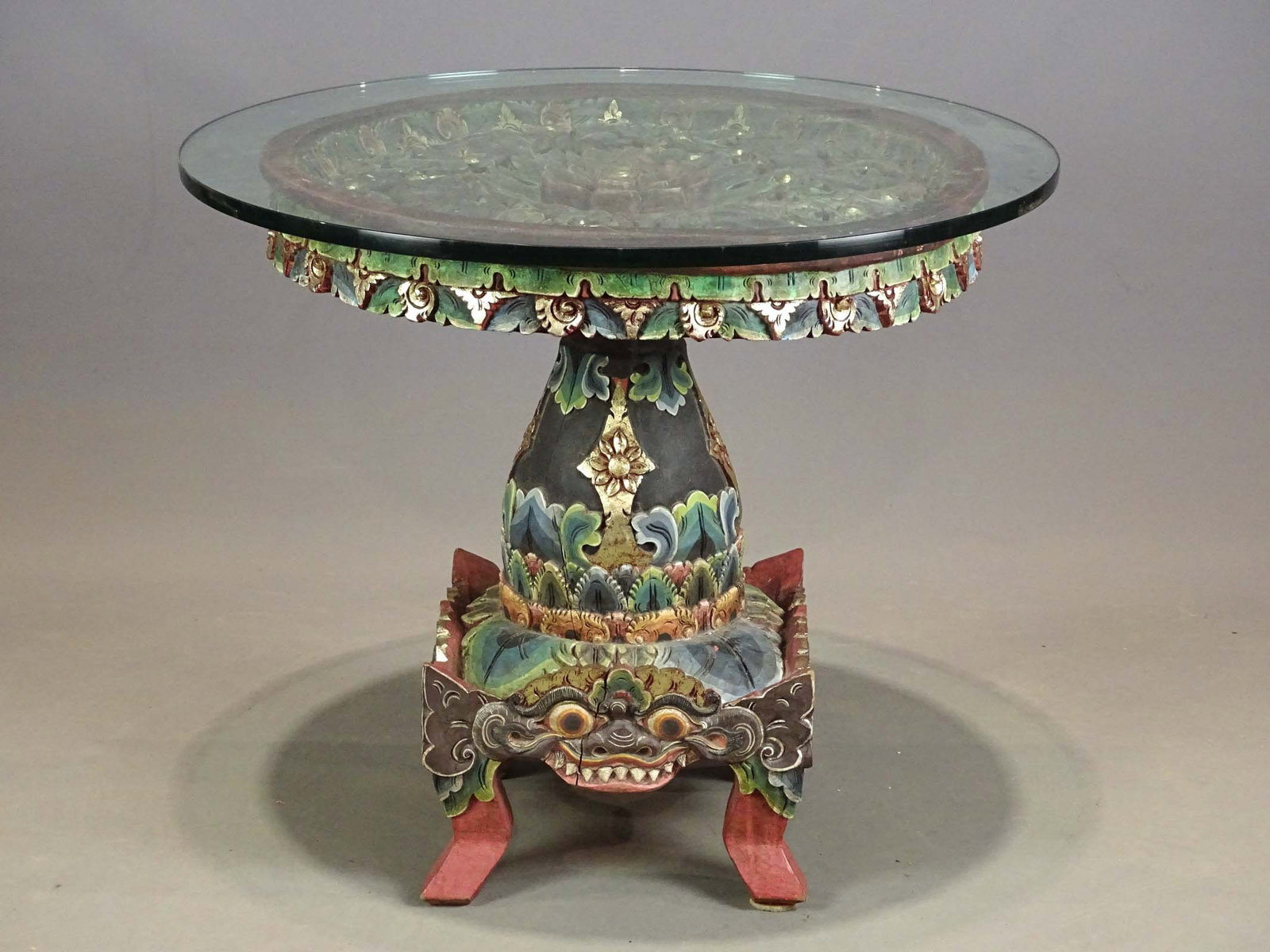 Indonesian Carved Table: Indonesian carved wooden polychrome painted glass top table. 34" D., 28" Ht..