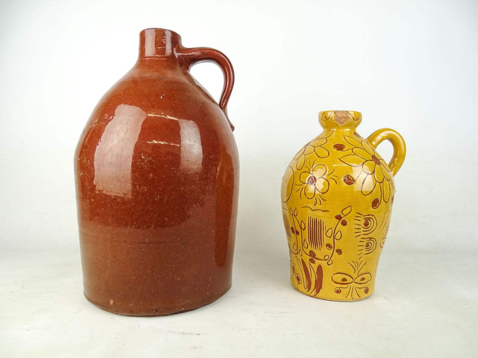 Lot of 2 Jugs: Lot of 2 jugs. Largest is 16" ht x 9" diameter base. Other is 12"ht x 5" diameter base. Chip on rim. Signed on the bottom.