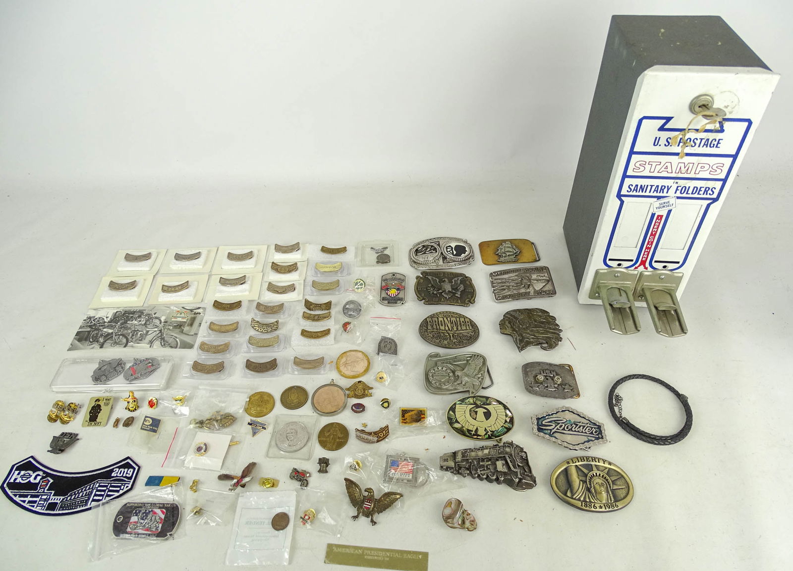 Stamp Dispenser: 20th Century stamp dispenser, lot of (10) commemorative belt buckles, box of motorcycle memorabilia. Mostly Harley Davidson.