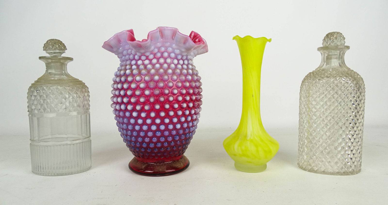 Glass Lot: Glass lot: Cranberry hobnail vase with ruffled rim (8" Ht), yellow bud vase (7 1/2" Ht), (2) clear patterned glass bottles with stoppers.