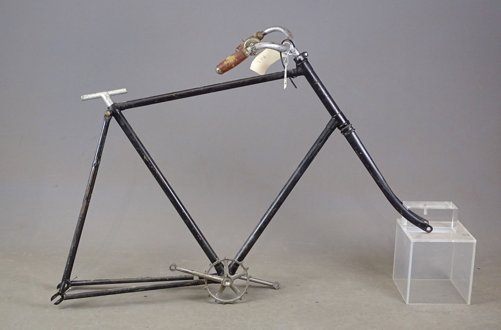 Unknown Maker Frame: Unknown maker (no headbadge): a bicycle frame with handlebars that have cork covered grips. It also has a chainr ing and a bottom bracket with ball bearings and pedal crank arms. It has a "T" seat