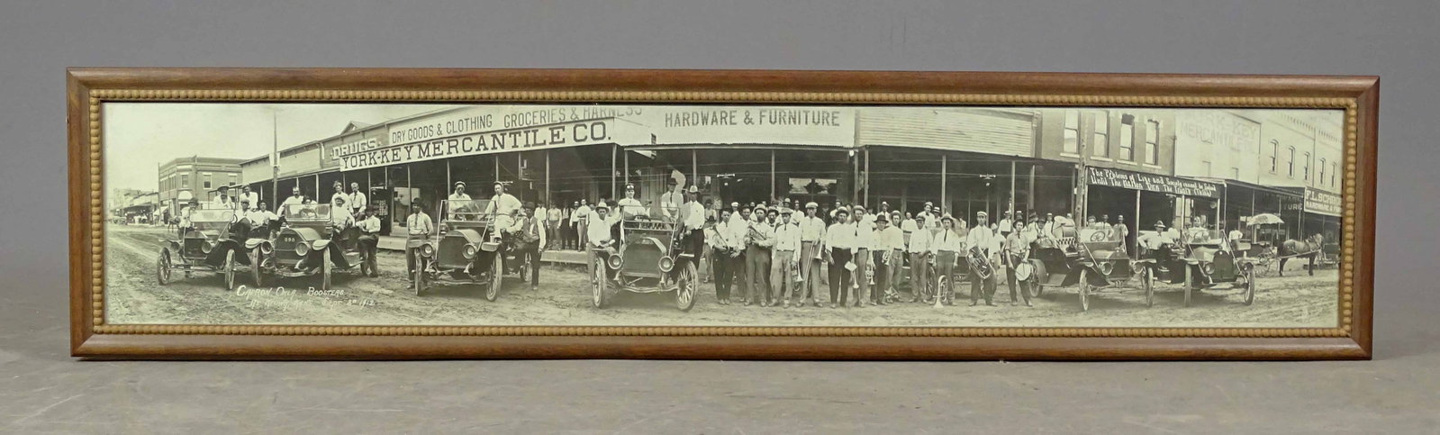 Yard Long Photograph: Early yard long photo "YORK-KEY MERCANTILE CO...". Features people lined up in front of stores with early automobiles. Overall in frame 10" x 46". Good condition. Capron Okla. Bootsteps at Kiowa Kans