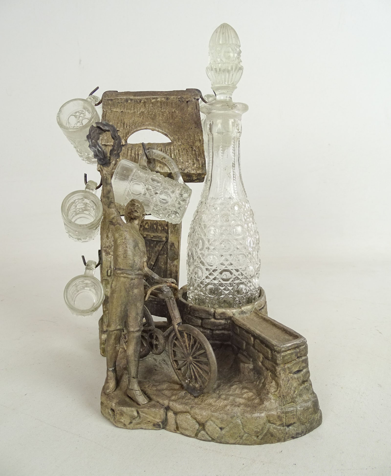 Decanter Set: 19th c. decanter set. Spelter metal statue with Victorian Wheelmen. Includes patter glass bottle and (5) mugs. 8 1/2" Ht... Good condition.