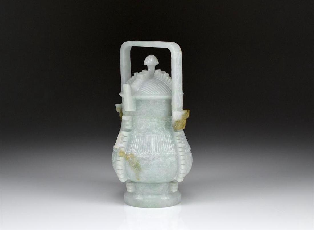 CHINESE ARCHAISTIC MANNER JADE YOU VESSEL: In the form of a Han dynasty bronze ritual wine vessel with carved decoration and swing handle, in a light celadon jade with minor russet inclusions. Height to top of handle 16.5cm (6 1/2 in.)