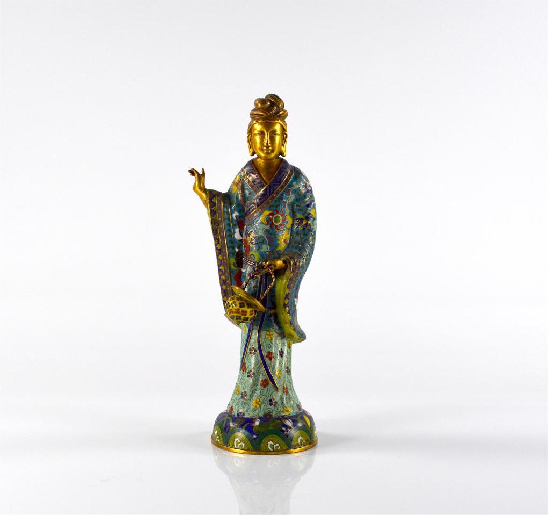 GILT BRONZE CLOISONNE ENAMELLED LADY FIGURE: The figure of a heavenly maiden, possibly Guanyin, shown standing in flowing robes holding a flower basket on one hand. The dress is decorated with Buddhist emblems. H. 31.1cm (12 1/4 in.)