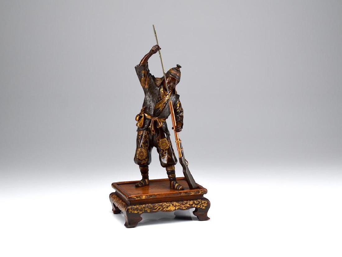 MIYAO EISUKE, MEIJI PERIOD GILT BRONZE OKIMONO: Of a warrior wearing a fur vest over richly brocaded clothes. Left hand holding onto a rifle while right hand in a loading motion. Feet affixed to typical Miyao-style wood stand decorated in gold taka