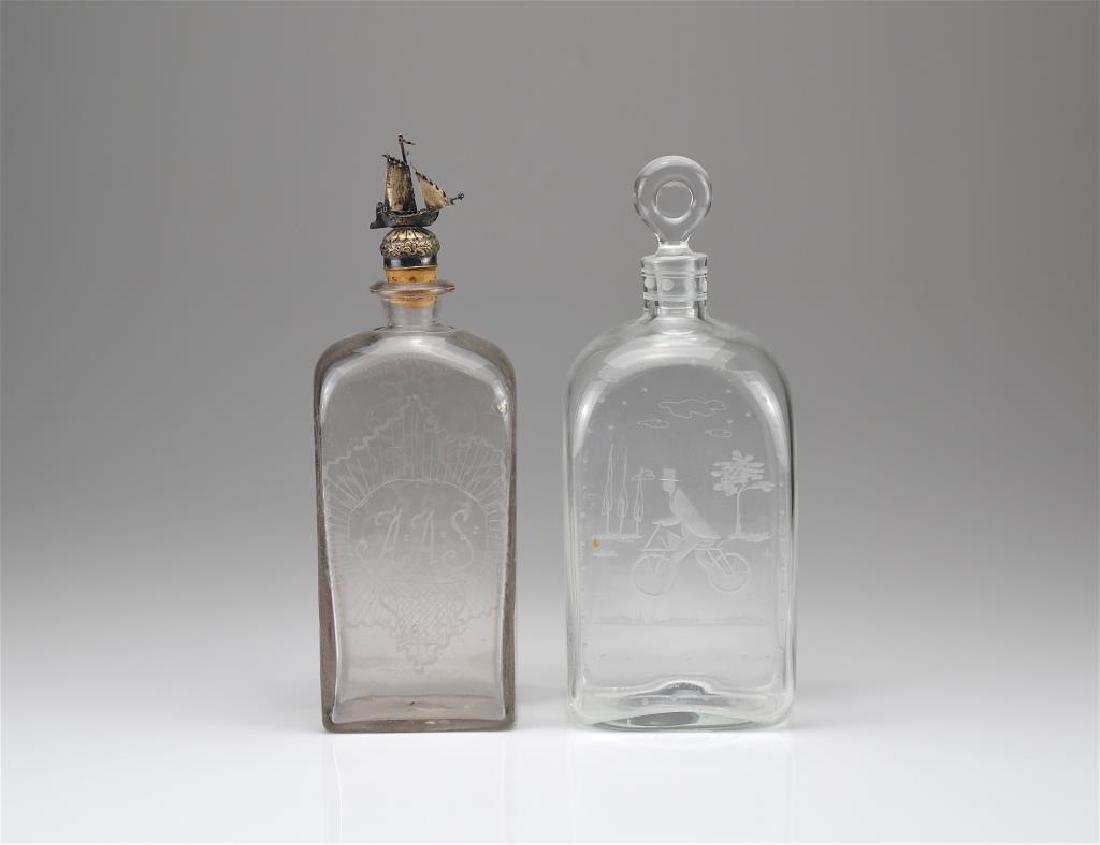 Two engraved glass decanters: One marked Holmegaard, K. Suanlund 18447-35 with etched decoration of a man in a top hat riding a bicycle. The other with Dutch silver ship stopper. H. of tallest: 26.7 cm (10 1/2 in.)