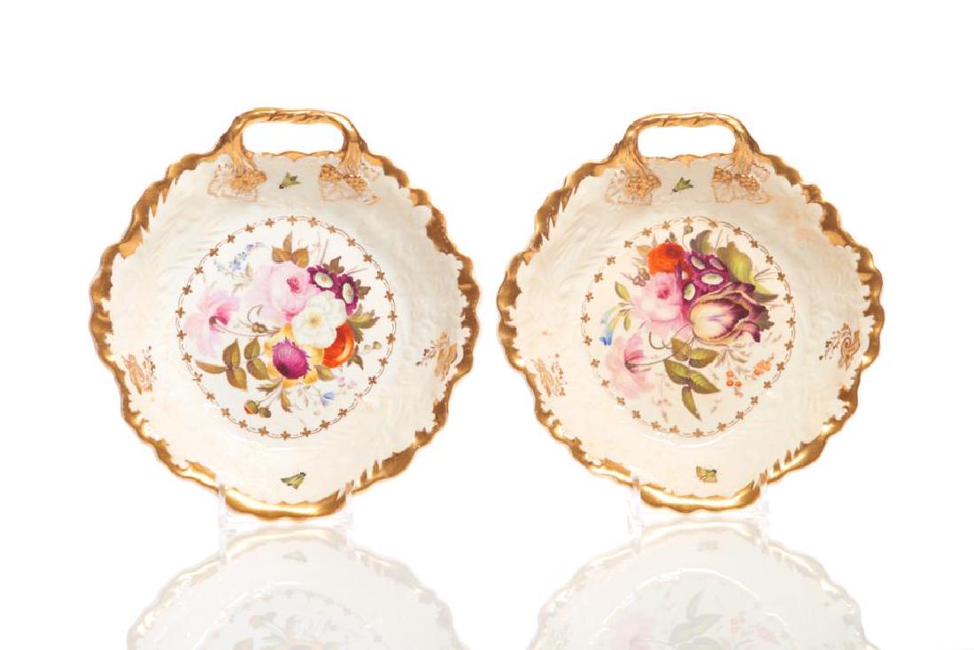 Pair of 19th C English hand painted dessert dishes: Each shallow bowl with a handle on one side, moulded border surrounding a central floral bouquet to center, gilt accents and butterflies. Early 19th C. Possibly Copeland or Spode. L.including handle: 