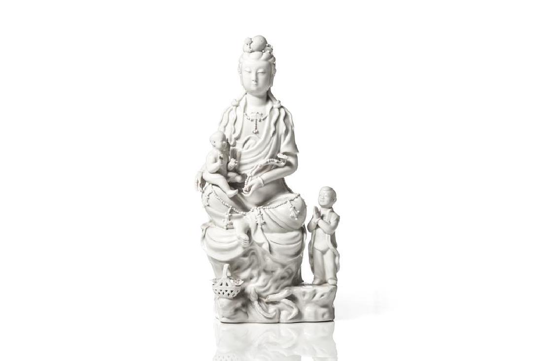 CHINESE DEHUA PORCELAIN GUANYIN GROUP: Overall glazed in blanc de chine white, with a seated Guanyin figure holding a boy and ruyi scepter, and attended by another boy. H. 33cm (13 in.)