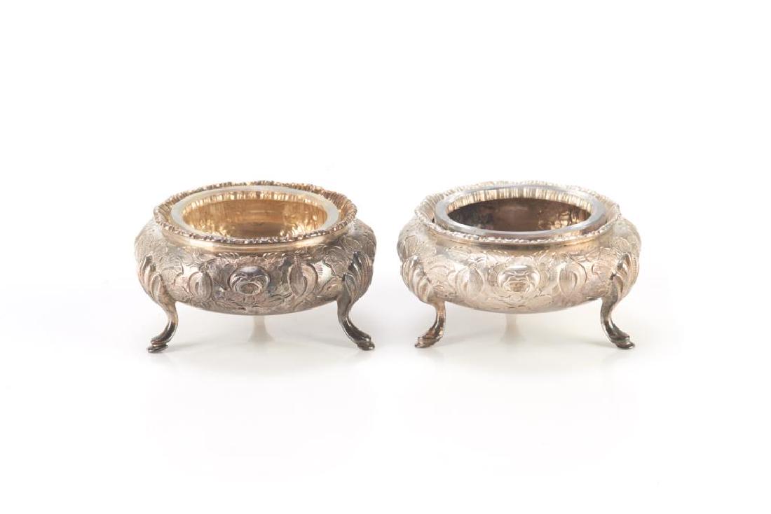Pair of English Victorian silver salts: Of typical form on three hoof feet with chased floral decoration. Sheffield, 1860. Martin, Hall and Co. 139g. 7 cm (2 3/4 in.)