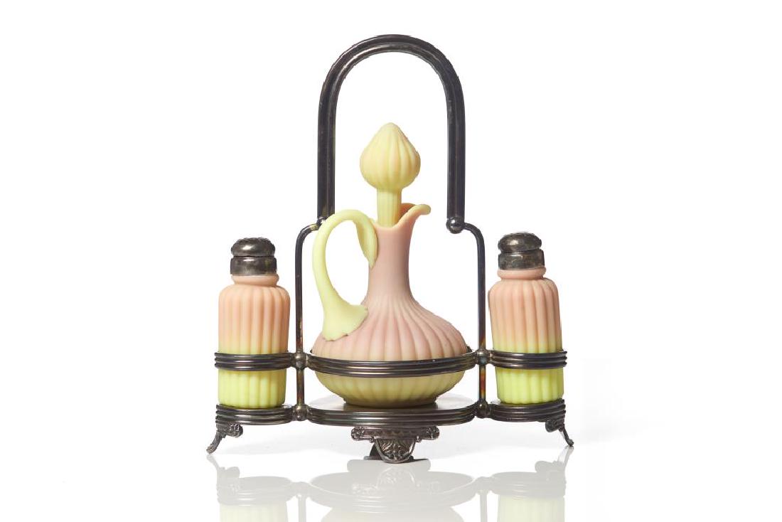 Burmese three piece glass condiment set: Including a cruet jug and salt shakers all with matte ribbed bodies, by Mt. Washington, with fitted American silverplated stand by Pairpoint. H of stand 25.4cm (10in)