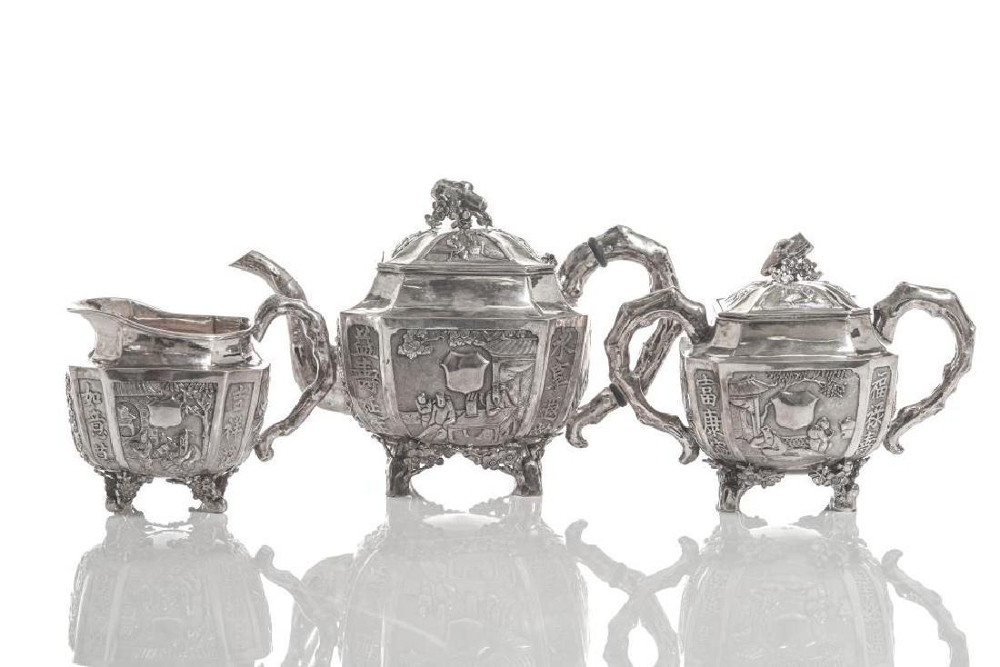 CHINESE EXPORT SILVER THREE PIECE TEA SET: Including a teapot, a sugar pot, and a cream jug. With hand raised repousse decoration of figural scenes, with natural tree trunk form finial, handle, feet, and spout, separated by auspicious Chinese