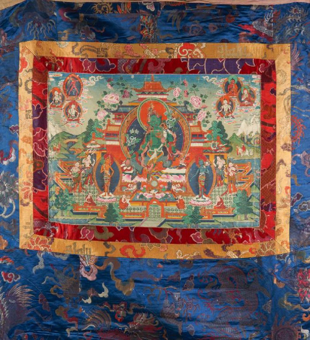 19TH C. PAINTED TIBETAN THANGKA OF GREEN TARA: The bodhisattva seated at center in lalitasana, the right hand extended in varada mudra, both arms holding the stems of lotus flowers, framed in a temple complex, flanked by attendants and twotriad gr
