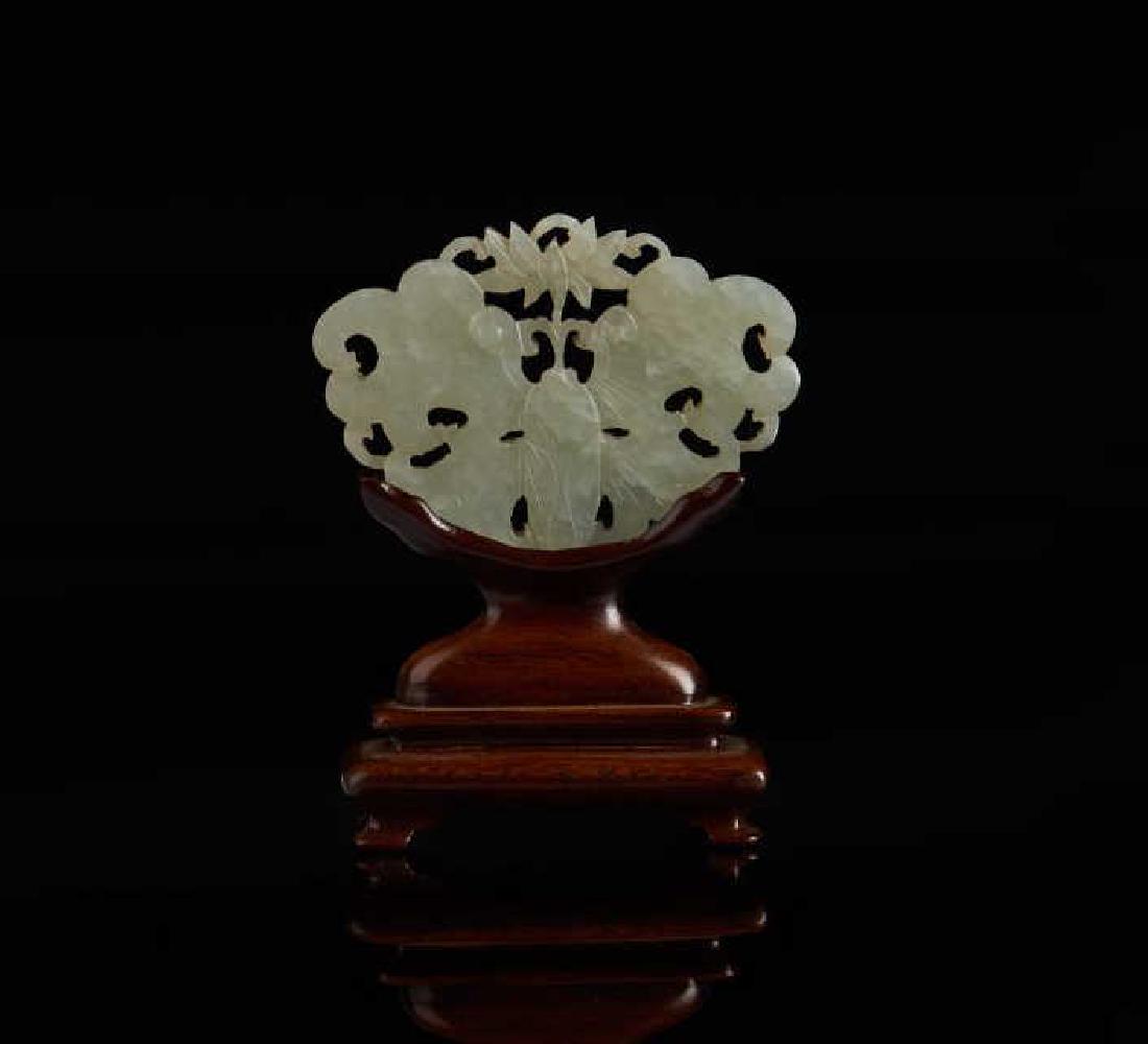 CHINESE CELADON JADE CARVED BUTTERFLY PLAQUE: Pale celadon jade. Carved in openwork style with a butterfly mouthing a lotus flower. Qing dynasty. W. 6cm (2 1/4 in.) Fitted wood base: H. 4.5cm (1 3/4 in.)Provenance: Chinese jades from the Ed Mirvi