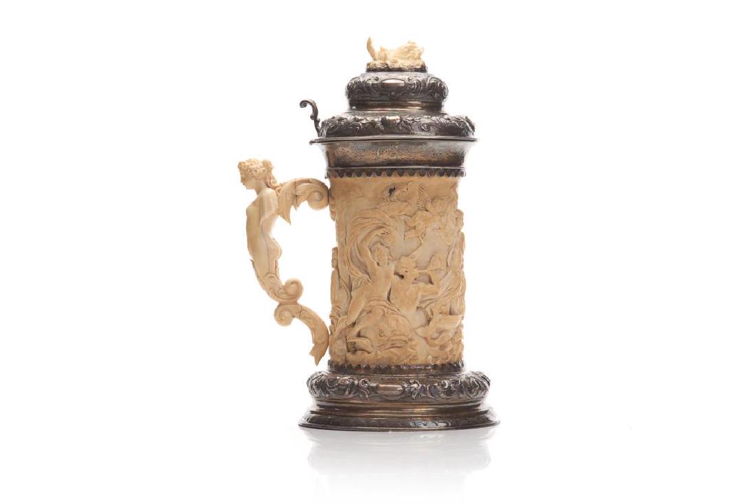 GERMAN SILVER AND CARVED NATURAL TANKARD: Carved in the round with a mythological motif of Poseidon, dolphins, nude figures and cherubs. Repousse silver mounts around the base and lid with natural carved finial of a dolphin. 19th C. H. 35cm (