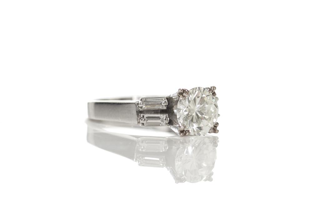 GOLD & DIAMOND SOLITAIRE RING: Chinese stamped 14k white gold band set with a central round brilliant cut diamond, 1.25 ct, and flanked by four baguettes. Total weight of diamonds 1.45 ct, total weight of ring 3.85 g. Size 4.Apprai