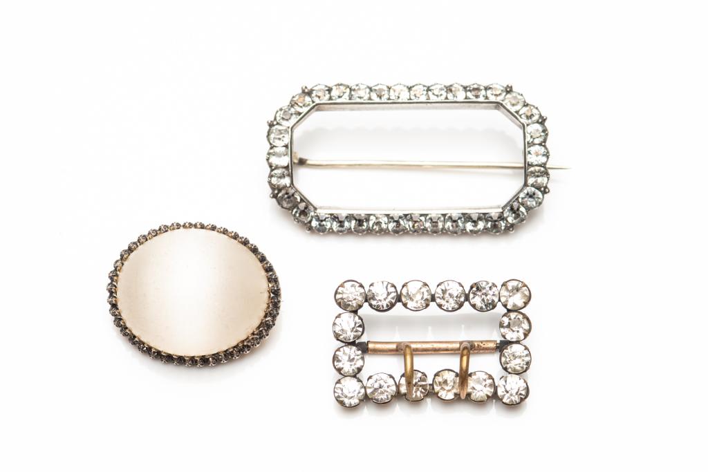TWO ANTIQUE BROOCHES & SHOECLIP: Three antique costume jewellery brooches. First brooch has a large opaque white cabochon stone in a gold and silver-toned prong setting. Second brooch is an open canted rectangle set with paste diamon