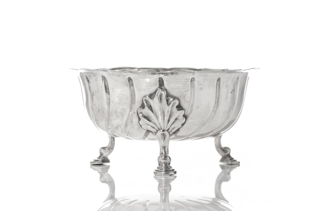 VICTORIAN ENGLISH SILVER FOOTED SUGAR BOWL: A scalloped edge bowl with swirling repousse details to the interior and raised on three hoof feet in the manner of an Irish Georgian example. Walter & John Barnard, London, 1889. Weight (total): 188g