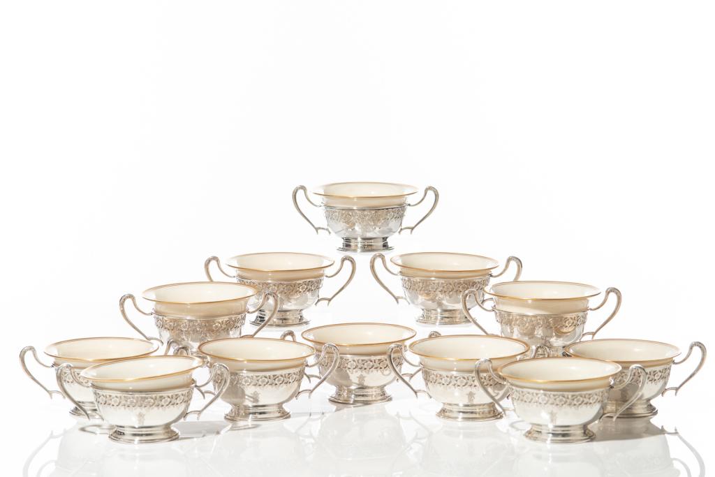 12 SILVER LINED LENOX PORCELAIN BOUILLON BOWLS: Twelve American Meriden Britannia silver bowls with Lenox porcelain inserts. Each silver frame with two handles and pierced floral decoration. 714g weighable silver Dia. porcelain bowl: 10.2 cm (4 in.