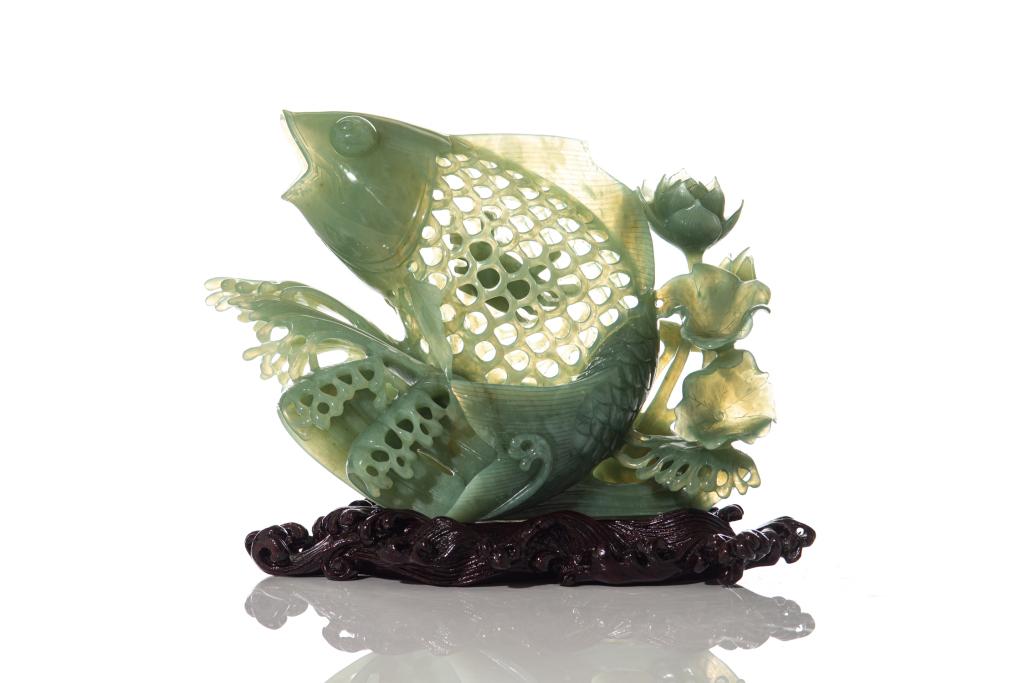 CHINESE NEPHRITE JADE CARVED FISH ON STAND: Carved as a carp leaping out of a wavy sea and accompanied by lotus flowers. The fish with pierced carved scales and a crab carved within the body. With fitted wave pattern wood stand. H. of carving: 