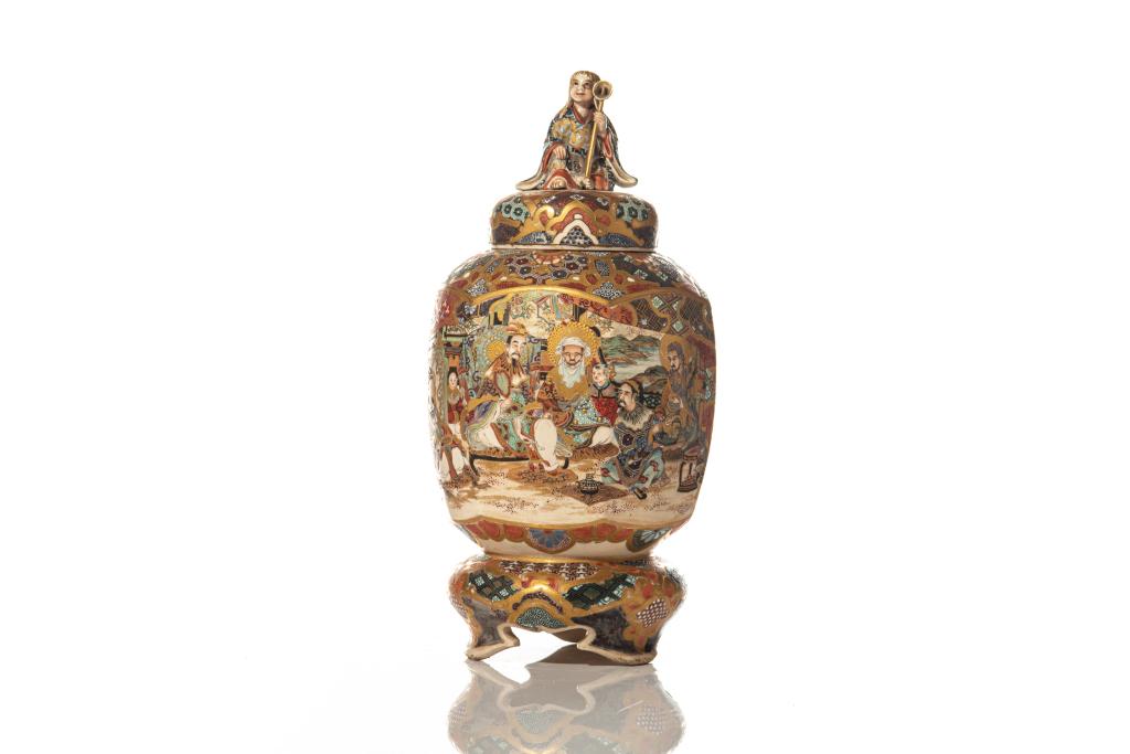 JAPANESE SATSUMA POTTERY HEXAGONAL JAR: The cover with a molded figure as finial. Hexagonal body standing on a tripod stand, painted with figural interior scenes. H. 28cm (11 in.)