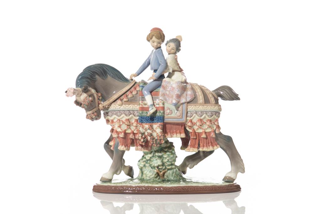 LLADRO VALENCIAN CHILDREN ON HORSE FIGURINE: Spanish 20th C. Depicting young boy and girl in traditional dress riding horseback, horse is dressed with an elaborate saddle. Stamp mark on underside. H. 26 cm (10 1/4 in) W. 27.5 cm (10 3/4 in)