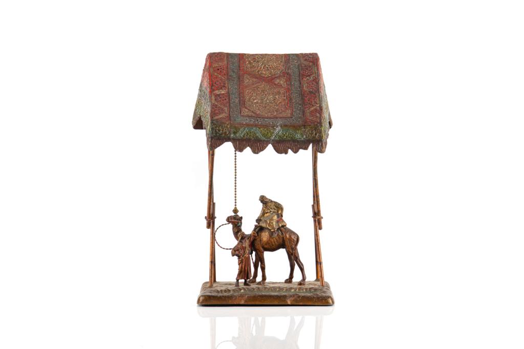 AUSTRIAN COLD PAINTED METAL FIGURAL TABLE LAMP: In the style of Franz Bergman, cold painted decorative lamp on a base metal with a central scene of two Middle Eastern figures meeting below a carpeted canopy, one atop a camel. Stamped to the undersi