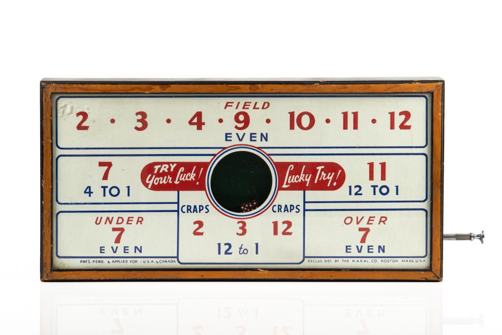 VINTAGE CRAPS DICE BOARD GAME: With side lever that shakes two dice in a central window. Marked exclusive distribution by the Karal Co. Boston Mass. U.S.A. H. 31 cm (12 1/4 in) W. 61 cm (24 in) D. 5.5 cm (2 1/4 in)