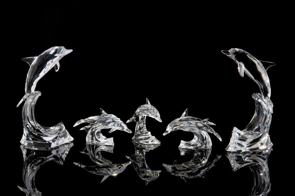 SWAROVSKI CRYSTAL COLLECTION OF DOLPHIN FIGURES: Group of five figurines, including: two large dolphins riding waves, two dolphin figures each swimming in a pair, and a smaller dolphin on a wave. H. of tallest 20 cm (7 7/8 in) Including one original