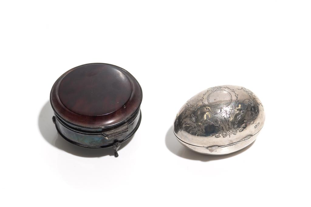 TWO ENGLISH VANITY PIECES: Comprising an egg shaped sterling silver box with a silk lined and gilded interior. George Nathan & Ridley Hayes, Chester, 1910. Together with a sterling silver box with a rosewood lid, raised on thre