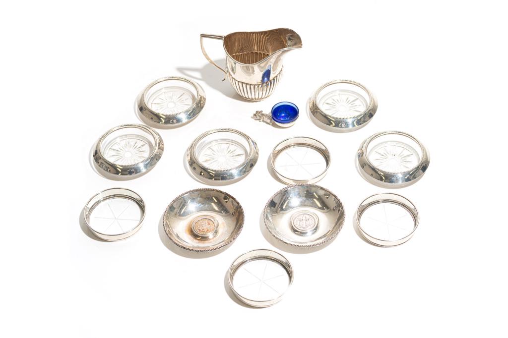 GROUP OF ASSORTED SILVER 314g: Including an English cream jug, a pair of Continental dishes with coin inserts, an Italian figural open salt with cobalt glass liner, and nine assorted coasters with glass inserts. Weight: 314g
