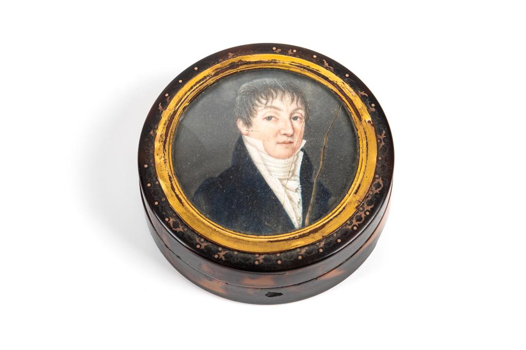 ANTIQUE GEORGIAN TORTOISESHELL SNUFF BOX: Circular box with gold plated lid encompassing a hand painted portrait miniature of a gentleman in formal dress. Dia. 6 cm (2 3/8 in) Condition noted. Bidders living outside of Canada are warned to pr