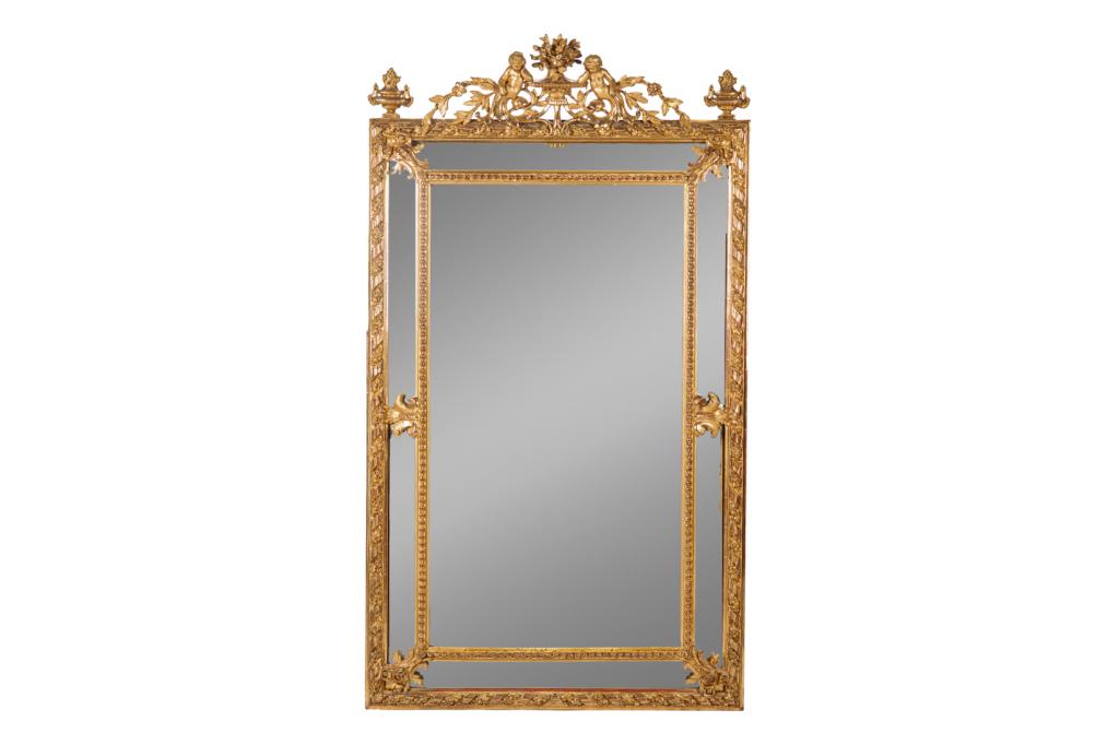 ANTIQUE CARVED GILTWOOD FRAMED MIRROR: French with gilded and gessoed frame and figural top. H. 68 1/2in. W. 38 3/4in.