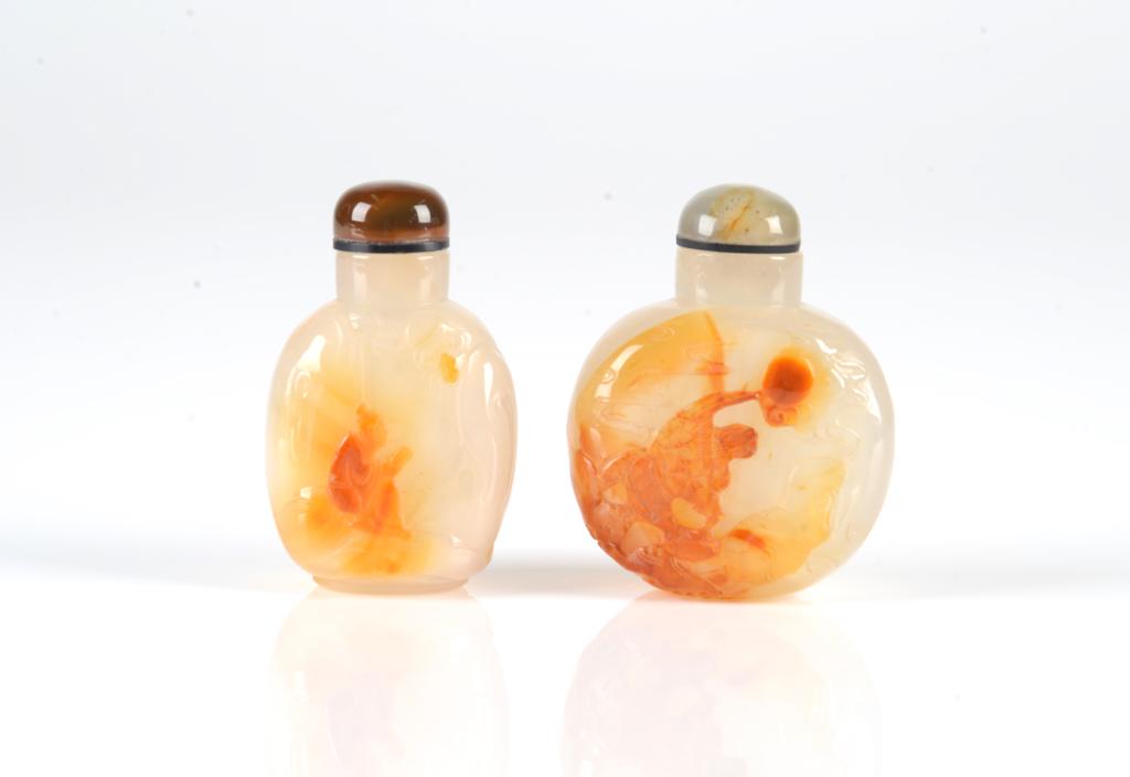 TWO CHINESE SHADOW CAMEO AGATE SNUFF BOTTLES: Each of a white body with carnelian burnt orange carved detail. The smaller depicting a seated scholar. The larger of an eagle on the rocks, both with matched agate stoppers. H of larger bottle 6cm (2