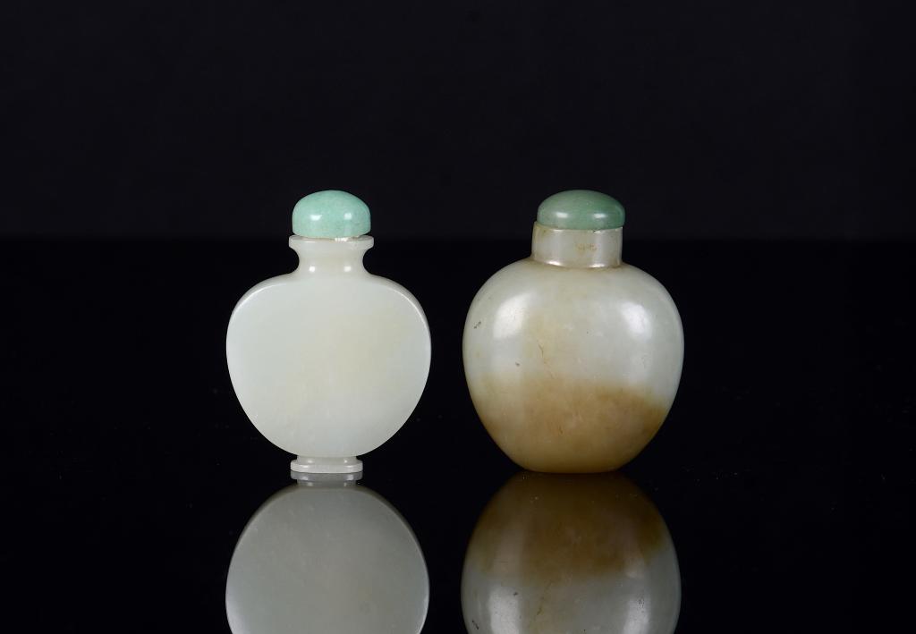 TWO CHINESE JADE SNUFF BOTTLES: Celadon green with flattened body and sides. The second of green bulbous jade form with russet skimming, base marked with collection number 51038.7. Both with jadeite stoppers, well hollowed interiors