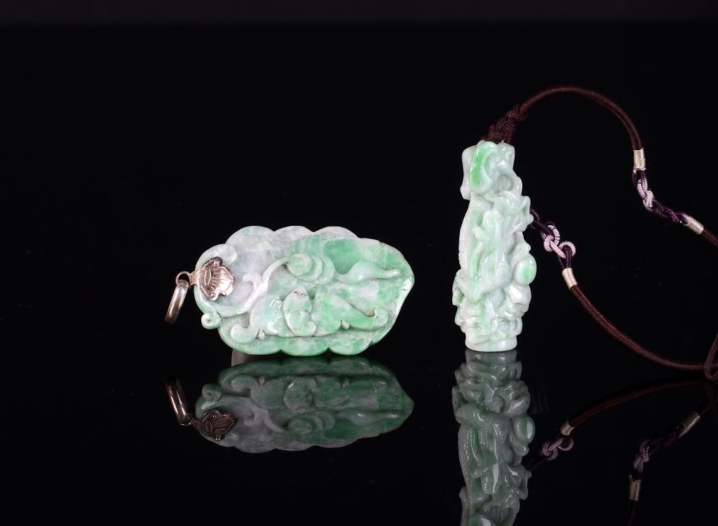 TWO CHINESE JADEITE PENDANTS: One carved with a bat and a string of money on a leaf. The other of a dragon climbing a cylindrical core. Larger: 5.5cm (2 1/8 in.) Condition report available upon request.