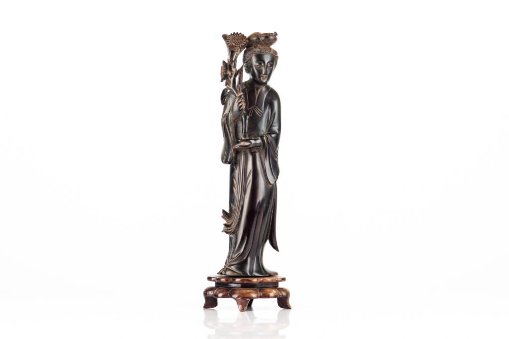 CHINESE AMBER CARVED LADY FIGURE: Carved as a standing lady holding a flowering branch. Attached to a wood base. Carving height: 29cm (11 1/2 in.) Height on stand: 33cm (13 in.) Condition report available upon request.