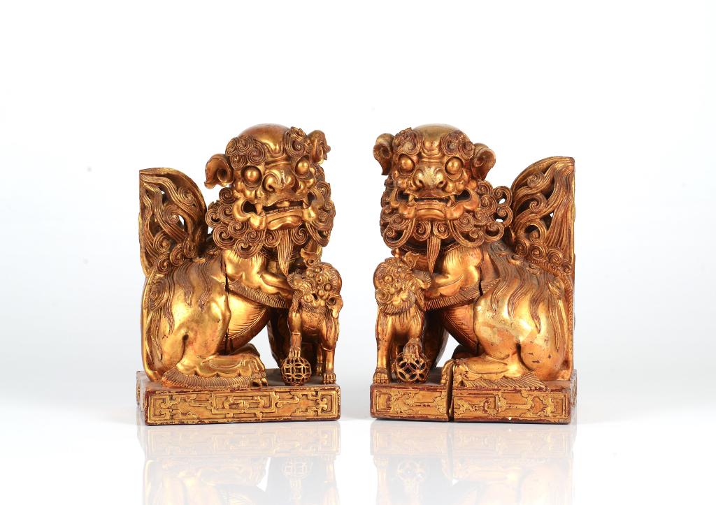 PAIR OF GILT & LACQUERED WOOD FU LIONS GROUP: Each carved as a mirroing image of the other, with details to hair patterns, chilong dragon decoration to base. Qing dynasty. H. 26.5cm (10 1/2 in.) Condition report available upon request.