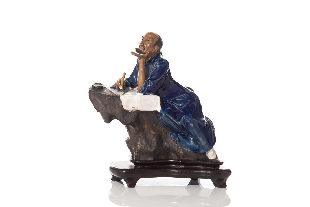 CHINESE SHIWAN POTTERY LITERATI FIGURE: Seated poet figure perched on a rock formation wearing blue glazed robe, with brush, paper, and inkstone present for calligraphy. Impressed seal mark to interior. With fitted wood stand. Heighton stan