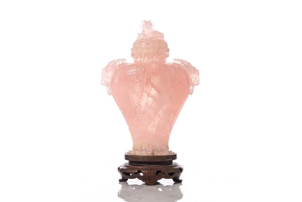 CHINESE ROSE PINK QUARTZ CARVED ORNAMENTAL VASE: Cover carved with a ram finial, pair of ram head and ring handles to shoulder. Body with shallow relief carvings of landscape scene. Fitted on wood stand with silver inlays. Height on stand: 17.5cm (7